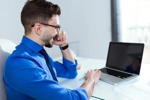 Jovem bonito trabalhando com laptop e telefone celular no escritório . — Fotografia de Stock