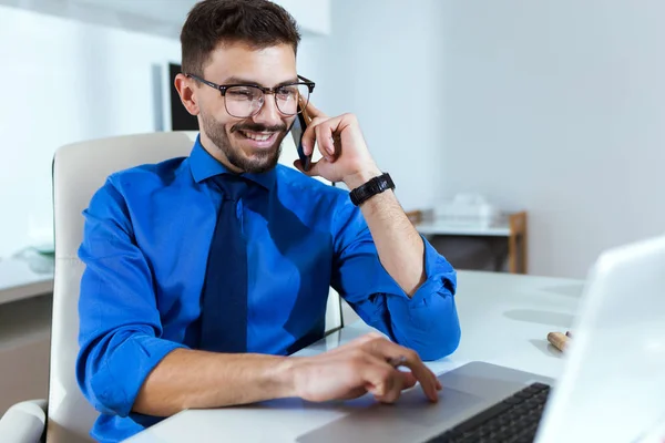 Jovem bonito trabalhando com laptop e telefone celular no escritório . — Fotografia de Stock