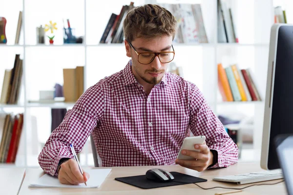 Όμορφος νεαρός επιχειρηματίας χρησιμοποιώντας το κινητό του τηλέφωνο στο γραφείο. — Φωτογραφία Αρχείου