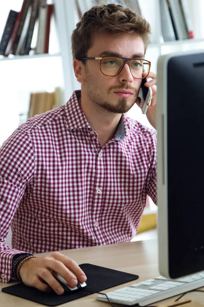 Beau jeune homme travaillant avec ordinateur portable et téléphone portable dans le bureau . — Photo
