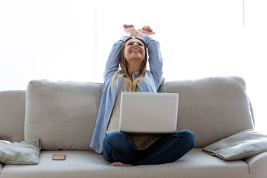 Güzel genç kadın evde laptop ile çalışırken bir başarı kutluyor.