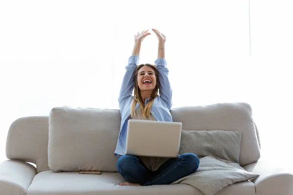 Piękna młoda kobieta świętuje sukces podczas pracy z laptopem w domu. — Zdjęcie stockowe