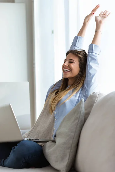 Όμορφη νεαρή γυναίκα που γιορτάζει το διάδοχο πρόγραμμα ενώ εργάζεστε με το φορητό υπολογιστή στο σπίτι. — Φωτογραφία Αρχείου