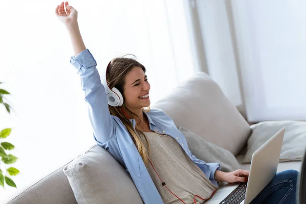 Schöne junge Frau, die zu Hause mit Laptop Musik hört. — Stockfoto