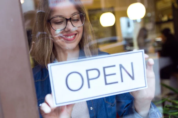 Beautiful young woman hanging the open sign in the store. — Stock Photo, Image
