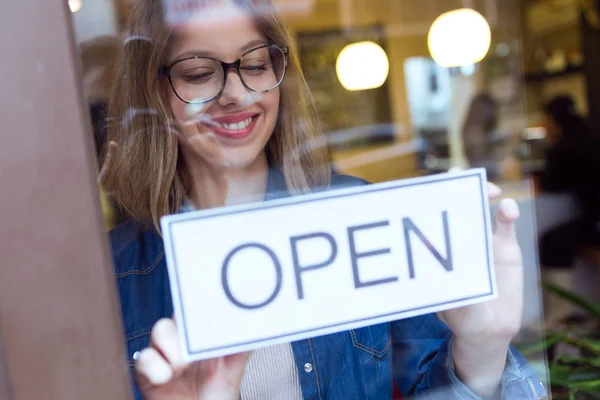 Mooie jonge vrouw, opknoping van het open teken in de winkel. — Stockfoto