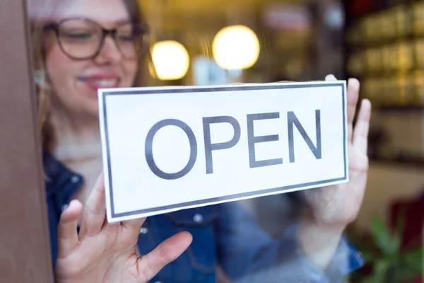 Beautiful young woman hanging the open sign in the store. — Stock Photo, Image