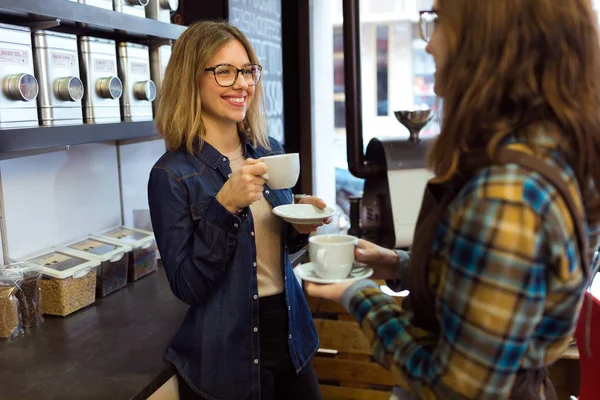 Két gyönyörű fiatal nő ivó kávé és beszél egy kávézóban. — Stock Fotó