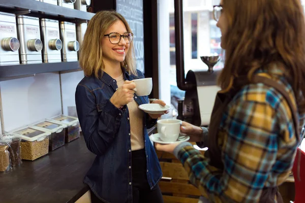 Two beautiful young women drinking coffee and talking in a coffee shop. — Stock Photo, Image