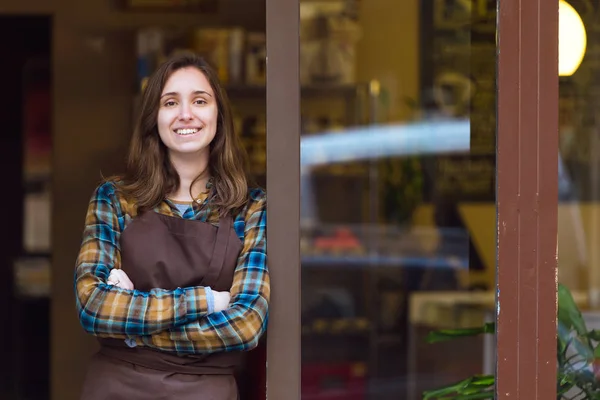 Mooie jonge verkoopster camera kijken en leunend tegen het kozijn van een biologische winkel. — Stockfoto