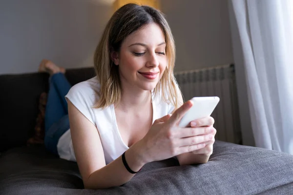 Beautiful happy young woman using her mobile phone at home. — Stock Photo, Image