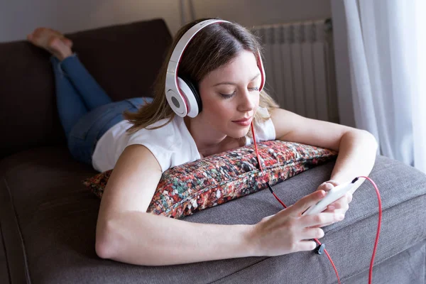 Mooie jonge vrouw, luisteren naar muziek met mobiele telefoon thuis. — Stockfoto