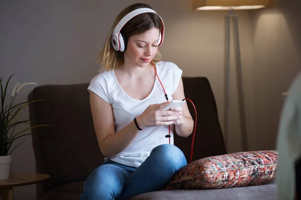 Mulher bonita ouvindo música com telefone celular em casa . — Fotografia de Stock