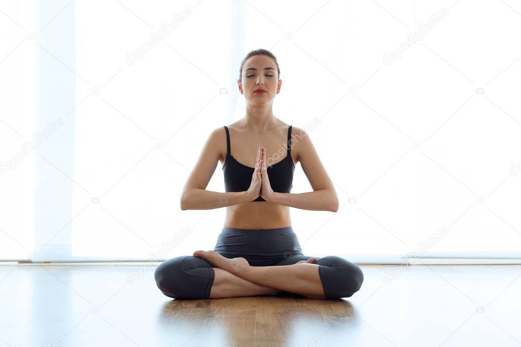 Beautiful sporty young woman doing yoga in lotus position at home.