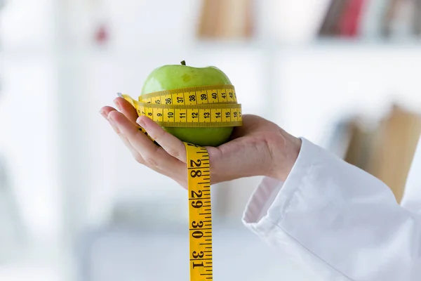 Female hand holding a green apple wrapped in a tape measure. — Stock Photo, Image