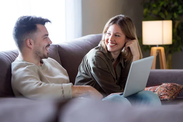 Pasangan muda yang cantik tersenyum menggunakan laptop mereka di rumah . — Stok Foto