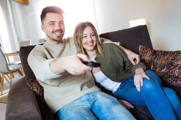 Piękna młoda uśmiechający się para oglądania telewizji w domu na kanapie. — Zdjęcie stockowe