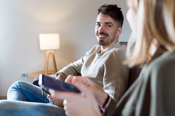 Όμορφη νέος χαμογελώντας ζευγάρι χρησιμοποιώντας το smartphone τους στο σπίτι. — Φωτογραφία Αρχείου