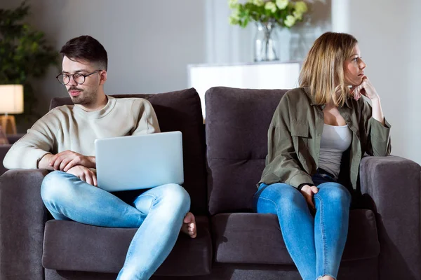 Pasangan muda yang marah duduk di sofa bersama-sama dan mencari sisi berlawanan di rumah . — Stok Foto