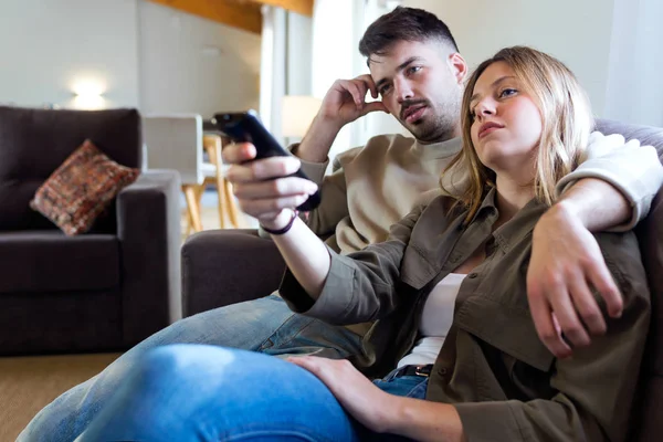 Bela jovem casal entediado assistindo TV no sofá em casa . — Fotografia de Stock