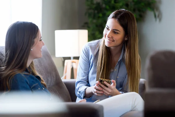 Två glada unga kvinnliga vänner samtala i vardagsrummet hemma — Stockfoto