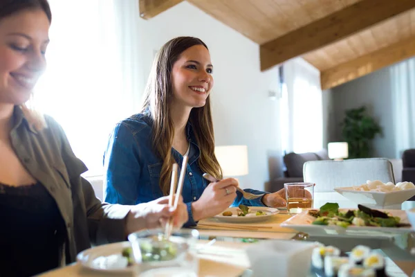 Dos hermosas mujeres jóvenes comiendo comida japonesa en casa . — Foto de Stock