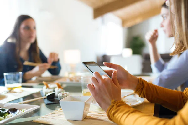 Jonge vrouw met behulp van haar mobiele telefoon terwijl het hebben van lunch met vrienden thuis. — Stockfoto