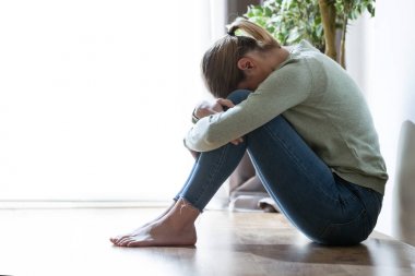 Mutsuz yalnız ve depresyonda genç kadın evde bacaklarının arasına yüzünü gizleme.