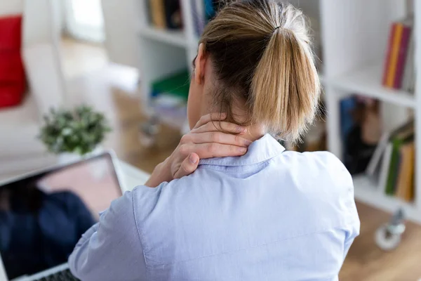 Müde junge Frau mit Nackenschmerzen mit ihrem Laptop zu Hause. — Stockfoto
