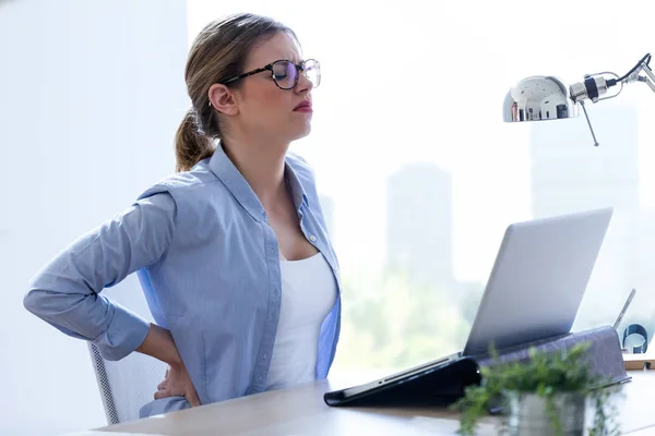 Trött ung kvinna med ryggsmärtor som använder sin laptop hemma. — Stockfoto