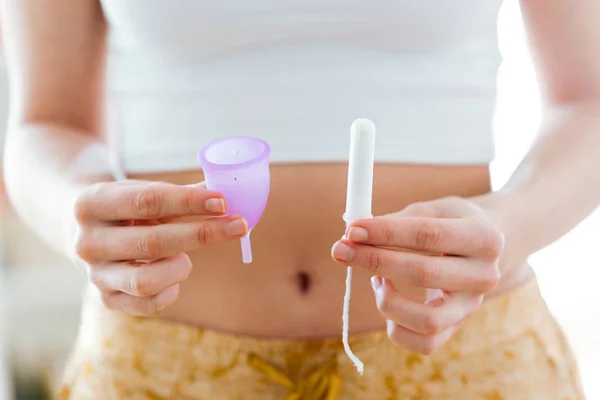 Manos de mujer joven sosteniendo diferentes tipos de productos de higiene femenina: copa menstrual y tampones. — Foto de Stock