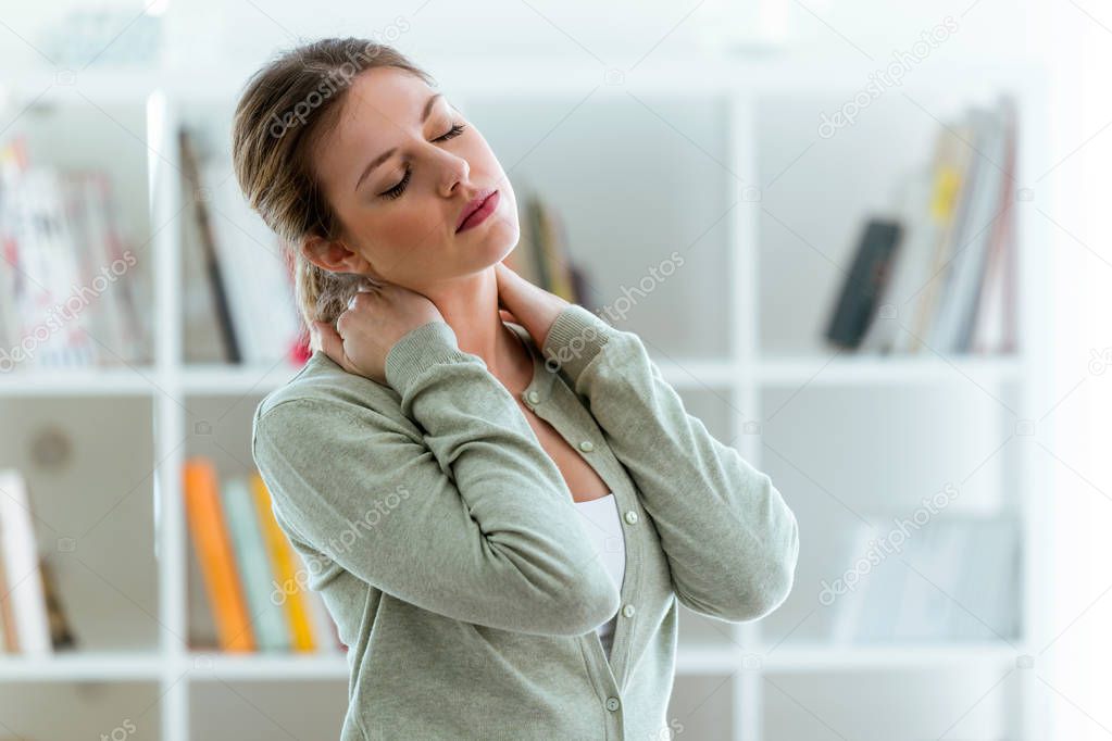 Tired young woman with neck pain at home.