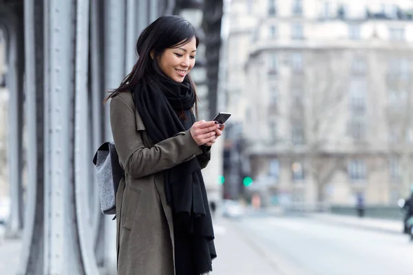 Sorridente asiatica giovane donna utilizzando il suo telefono cellulare in strada . — Foto Stock