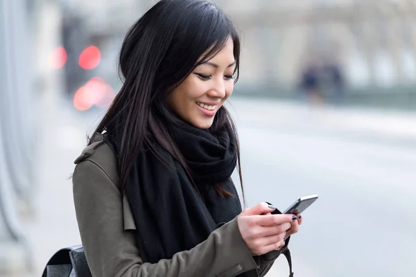 Lächelnde asiatische junge Frau mit ihrem Handy auf der Straße. — Stockfoto