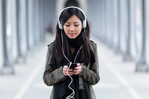 Muito asiático jovem mulher ouvindo música com seu smartphone na rua . — Fotografia de Stock