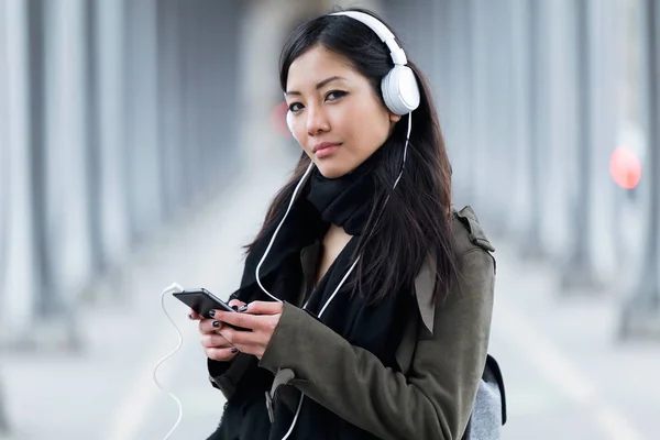 Bastante asiática joven mujer escuchando música y mirando a la cámara en la calle . — Foto de Stock
