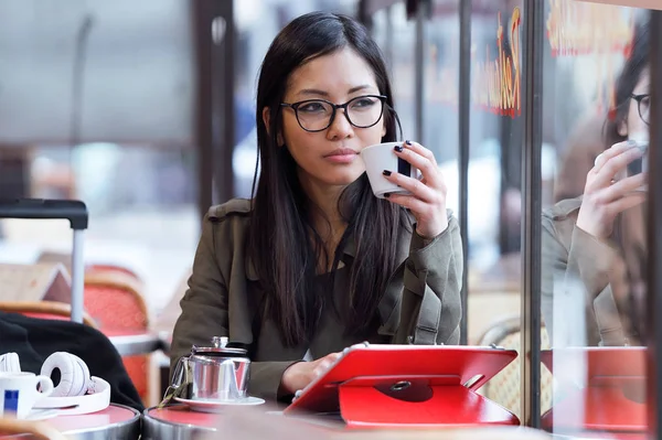 Hermosa joven mujer asiática usando su tableta digital mientras bebe café en la cafetería . — Foto de Stock