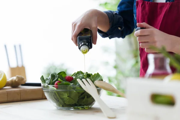 Junge Frau würzt den Salat zu Hause in der Küche mit Öl. — Stockfoto