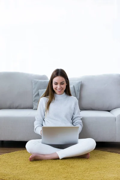 Bella giovane donna che utilizza il suo computer portatile mentre seduto sul pavimento a casa . — Foto Stock