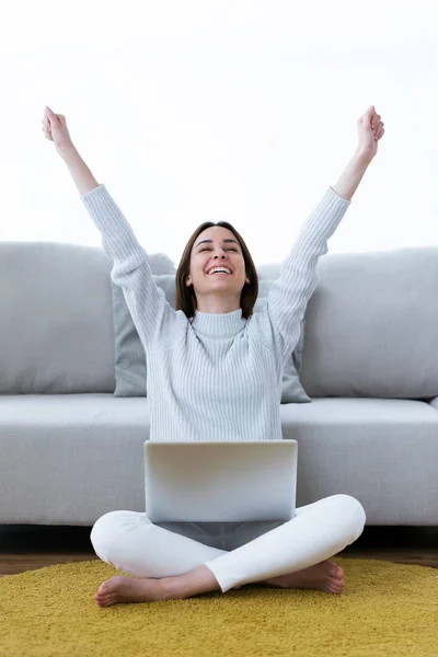Bella giovane donna che celebra un successo mentre lavora con il computer portatile a casa . — Foto Stock