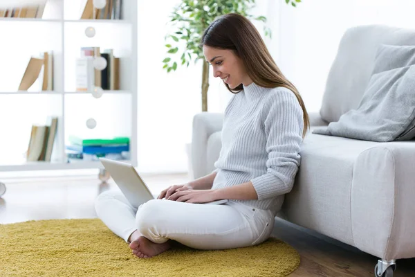 Hübsche junge Frau benutzt ihren Laptop, während sie zu Hause auf dem Boden sitzt. — Stockfoto