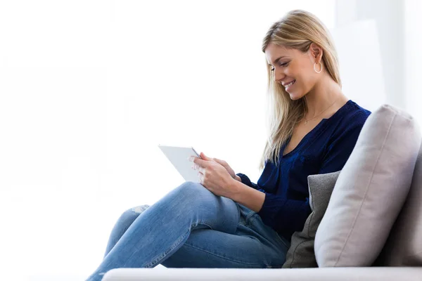 Lächelnde junge Frau mit ihrem digitalen Tablet, während sie zu Hause auf dem Sofa sitzt. — Stockfoto