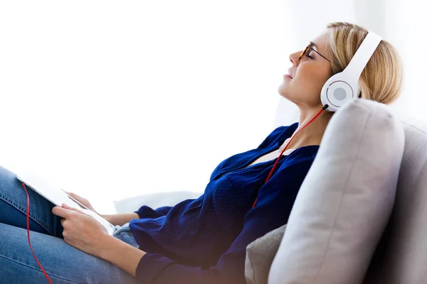 Schöne junge Frau, die zu Hause mit ihrem digitalen Tablet Musik hört. — Stockfoto