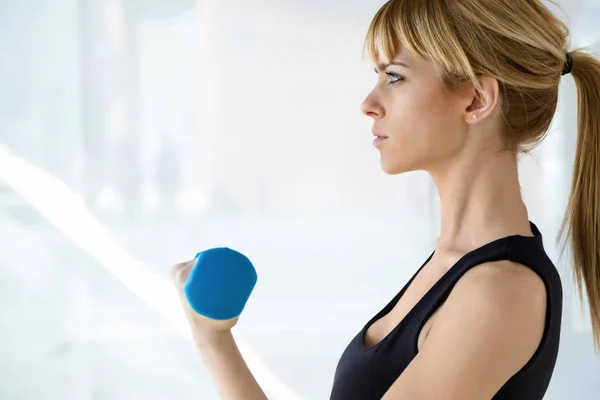 Jeune femme sportive faisant de l'exercice musculaire avec haltères bleues dans la salle de physio . — Photo
