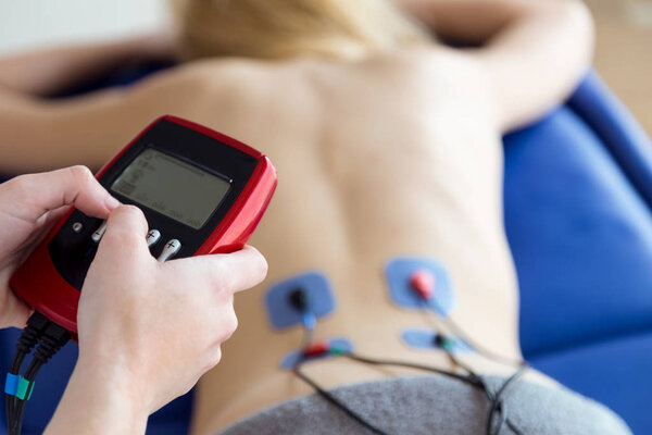 Young physioterapist applying electro stimulation in physical therapy to a patient in physio room.