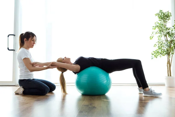 Fisioterapeuta ayudando al paciente a hacer ejercicio sobre la pelota de fitness en la sala de fisioterapia . — Foto de Stock