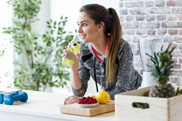 Jeune femme sportive regardant latéralement tout en buvant du jus de citron dans la cuisine à la maison . — Photo