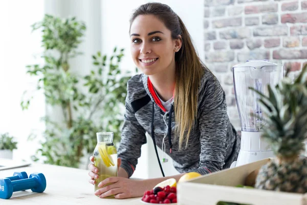 Jeune femme sportive regardant la caméra tout en buvant du jus de citron dans la cuisine à la maison . — Photo
