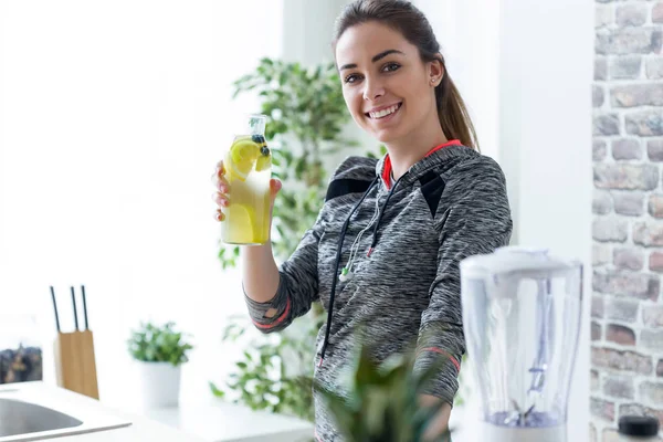 Jeune femme sportive regardant la caméra tout en buvant du jus de citron dans la cuisine à la maison . — Photo