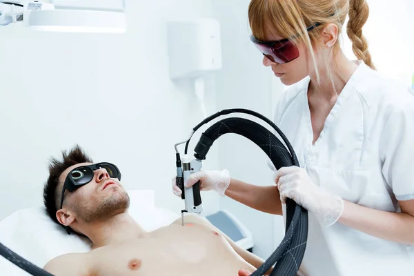 Young beautician removing torso hair with a laser to her client in the beauty salon. — Stock Photo, Image